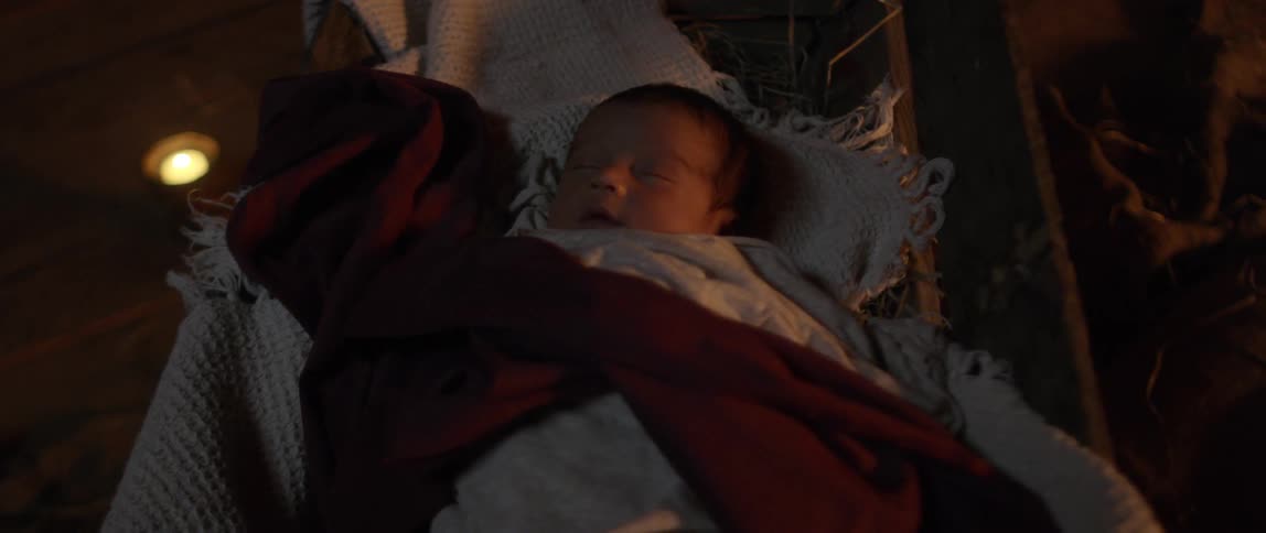 A newborn baby is asleep in a manger and covered in blankets