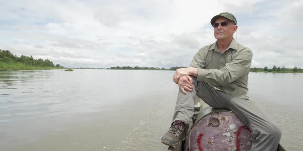 A older man sits on a powered dinghy as it moves down a wide river