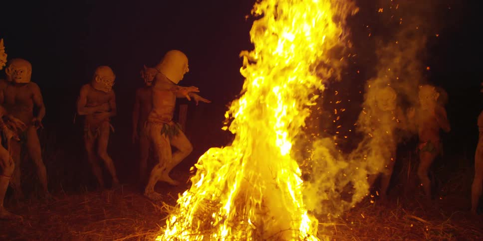 Tribal men in masks dance around an outdoor fire