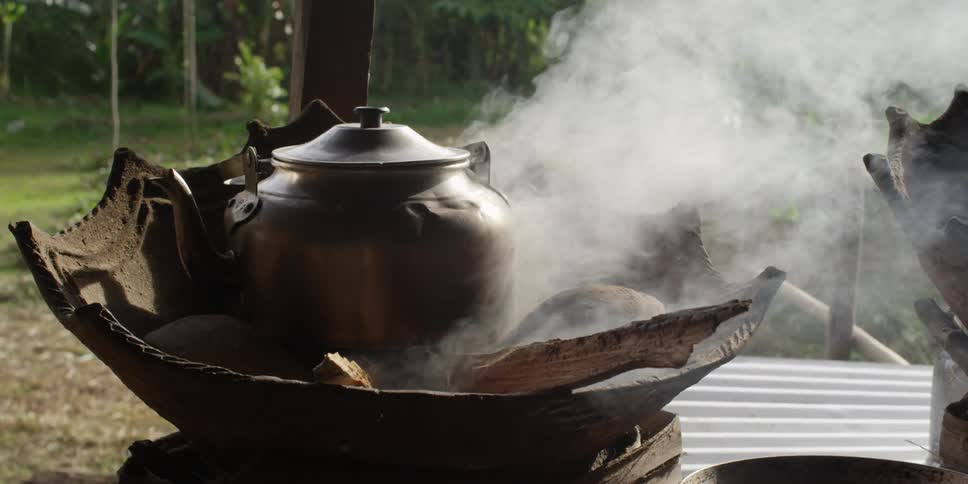 A kettle sits on stones in a smoking fire pit