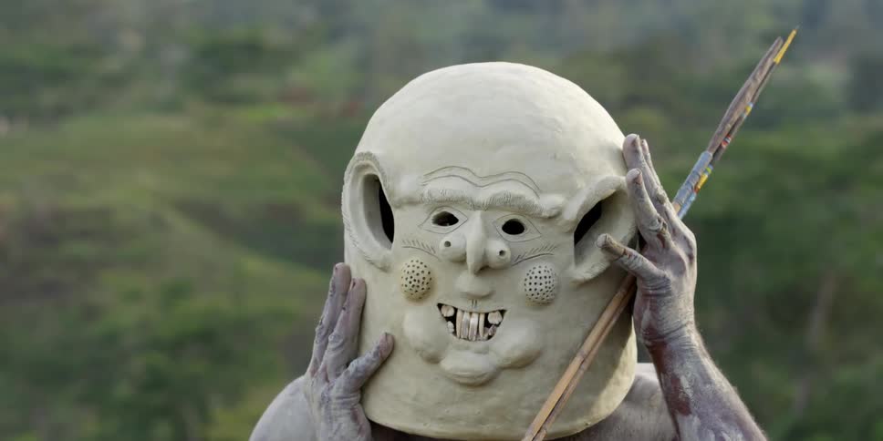 African man putting on a large clay mask