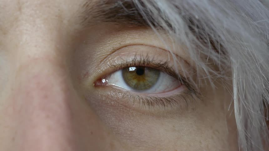 The droopy eye of a woman staring directly at the camera without blinking