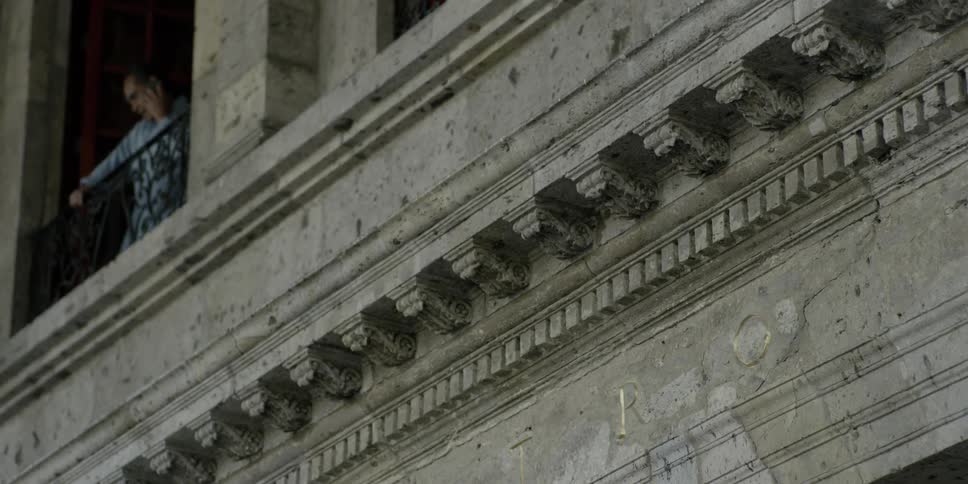 A man standing on a second floor balcony talking on a phone