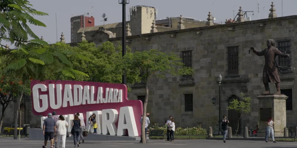People walk along the street in front of a large building