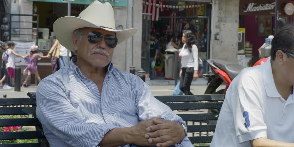 An old man in a cowboy hat sits on a bench