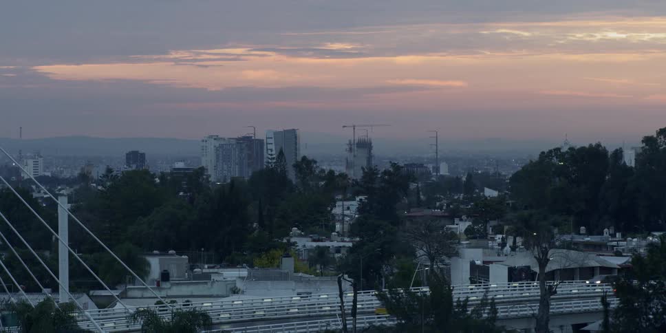 Vehicles drive along freeway near buildings at sunset