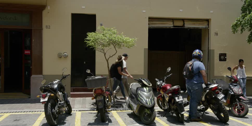 A man wearing a backpack and helmet gets off his motorcycle parked next to other bikes