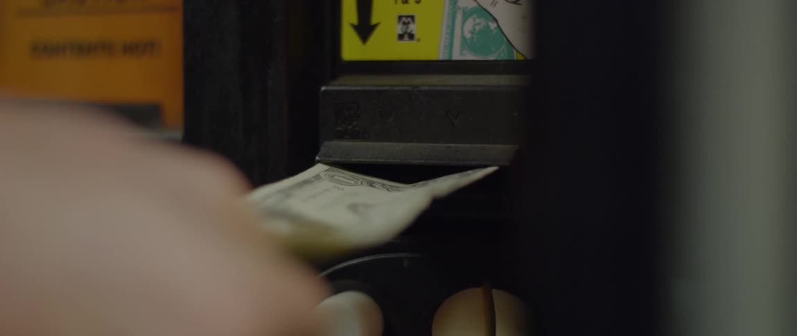 A person puts a one dollar bill into a vending machine