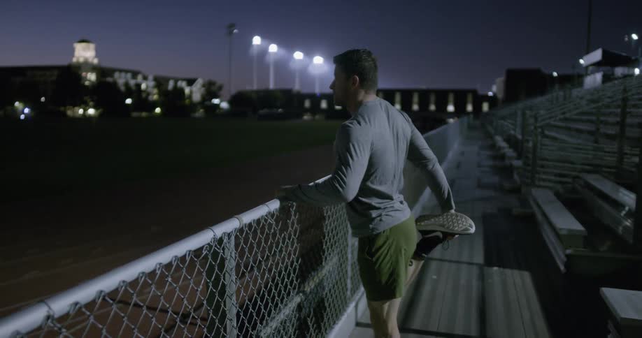 A man stretches at the bottom of some bleachers