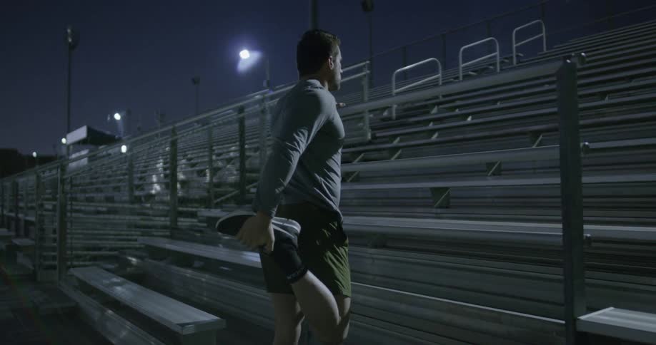 Man stretches while standing at base of bleachers