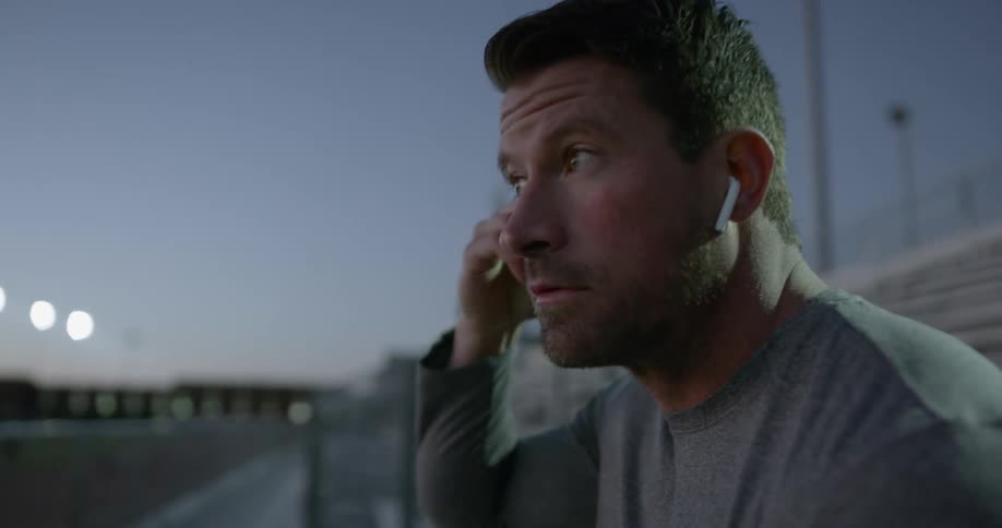 A man sitting on bleachers putting on earbuds