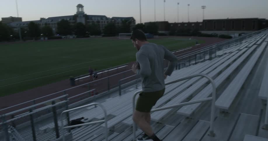 A man jogs down stadium steps past empty bleacher seats toward the track and field