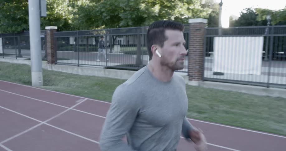 A white man in a gray shirt runs on a race track