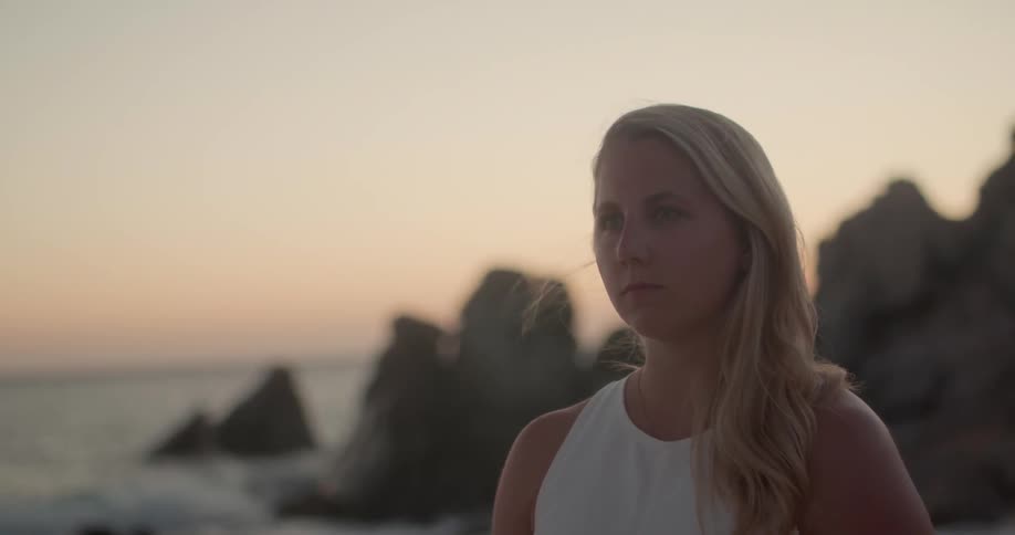 A white woman brushes her hair with her hand while standing on a beach