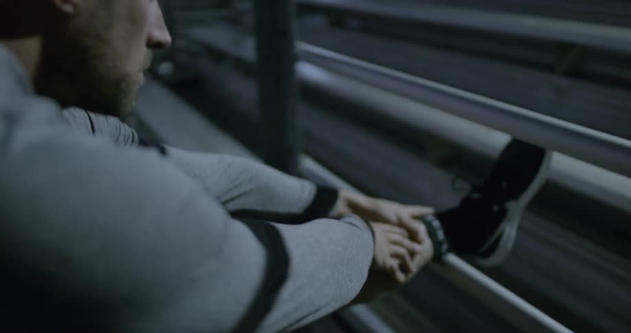 A man stretches his leg against a fence near bleachers