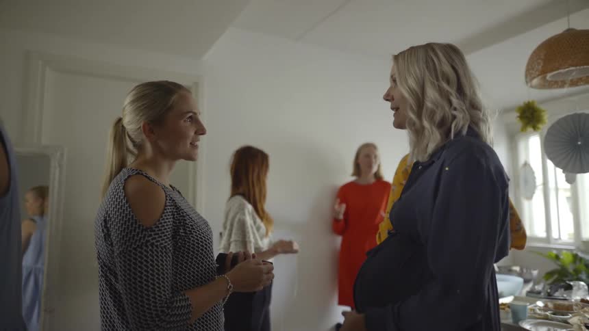 Two blonde white woman talk in a living room