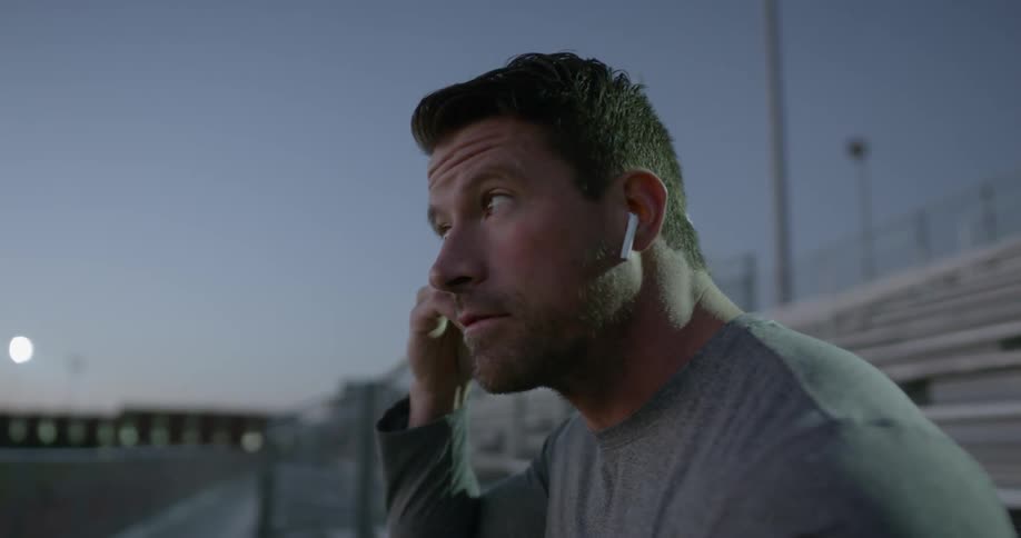 A man puts earbuds in his ears while sitting on outdoor bleachers