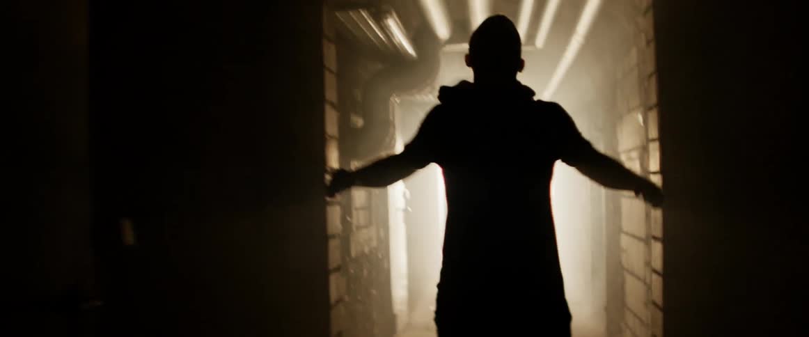 A man walking down a hallway with blinking lights while stretching his shoulders and neck