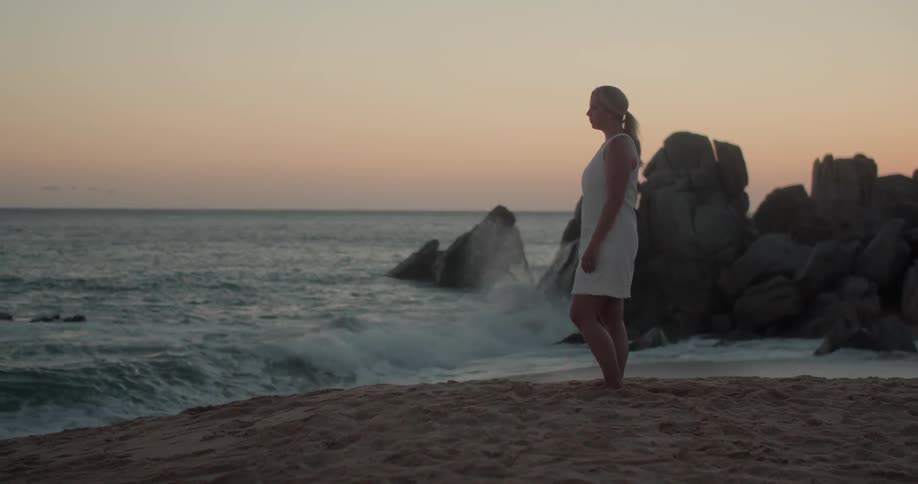 A woman standing on the beach looking at the ocean