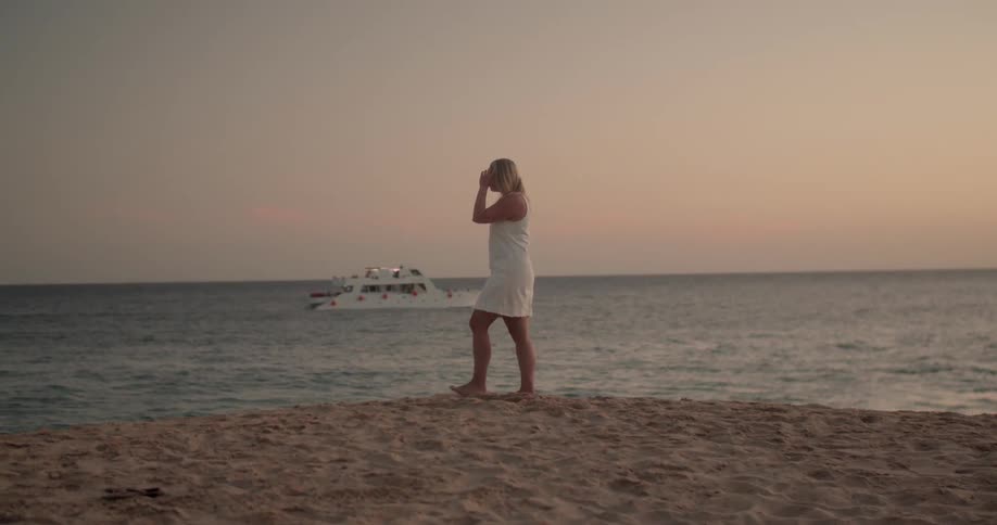 Woman walks along beach as yacht passes