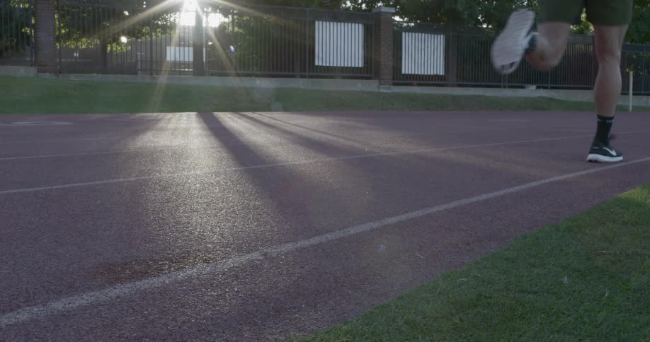 A male running on a track near fencing outside