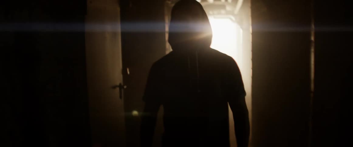 A backlit man walks down a dark hallway