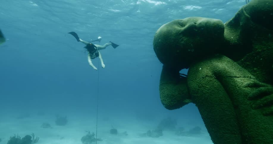 Woman scuba diving near fish and underwater statue