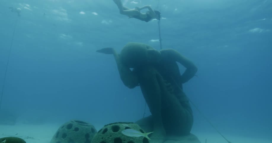 A statue of a person underwater while a woman swims