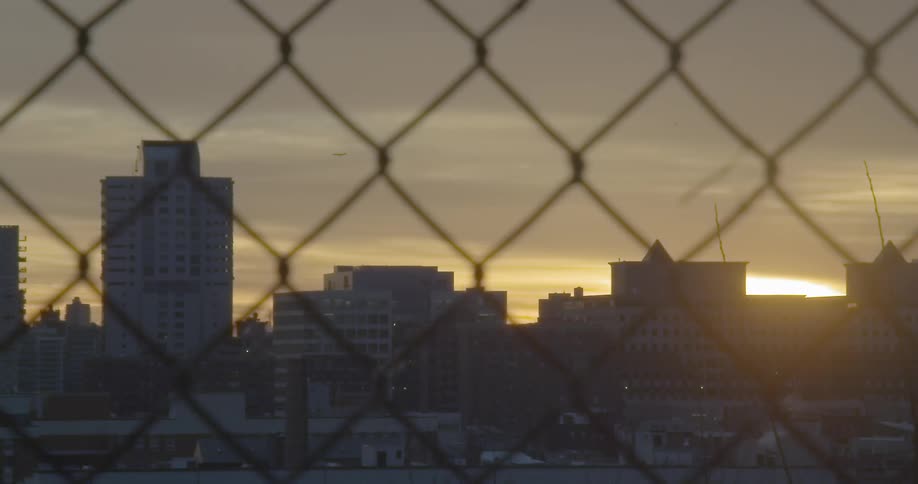 City buildings and sunset seen through a chain link fence