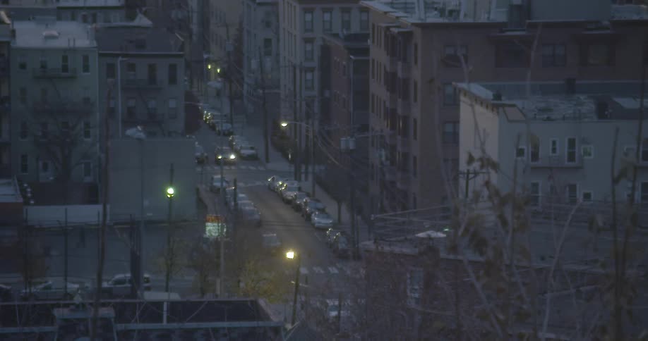 Cars driving down a street in an urban neighborhood in the evening