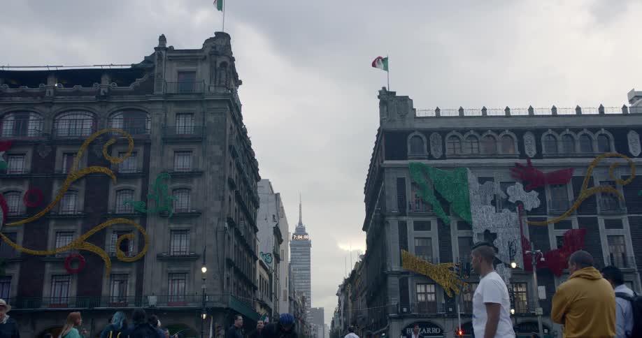 A crowd walks in front of tall buildings in a city on a cloudy day