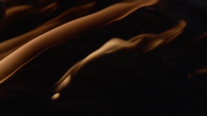 A gloved hand brushes over rolling golden flames