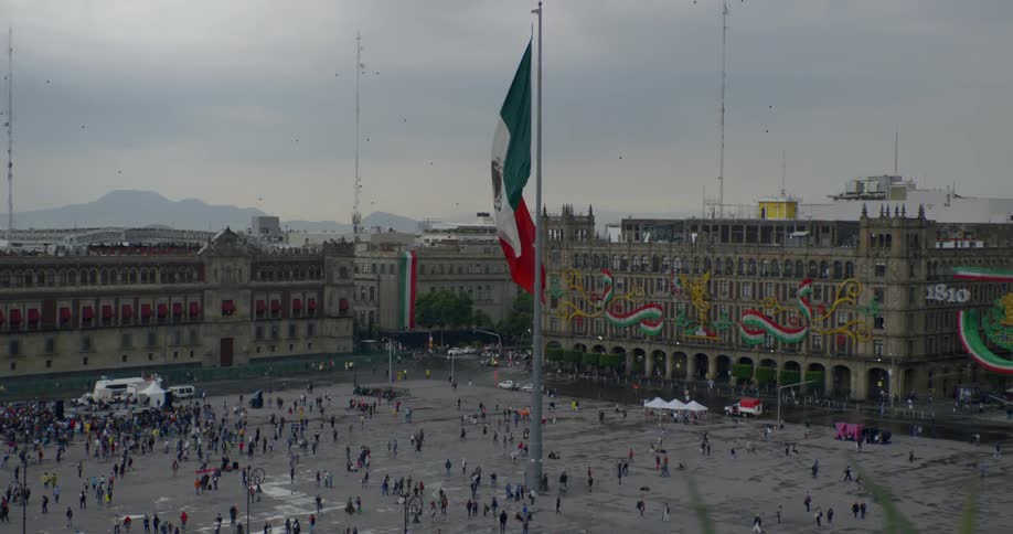 Mexican flag waves over plaza full of pedestrians