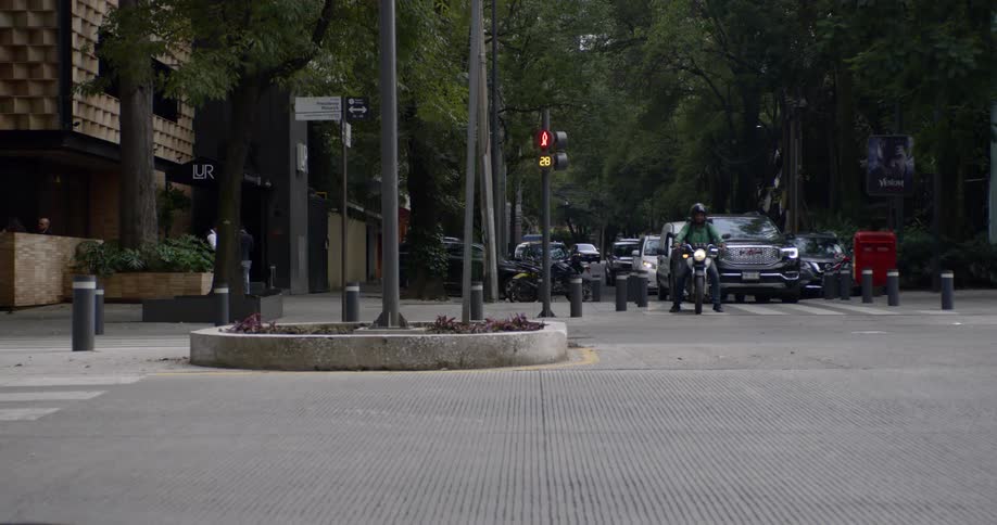 A motorcycle and cars wait at an intersection as other cars pass in both directions