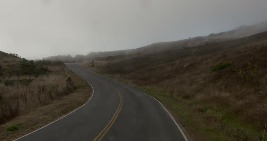A road curves around a hill covered in brush
