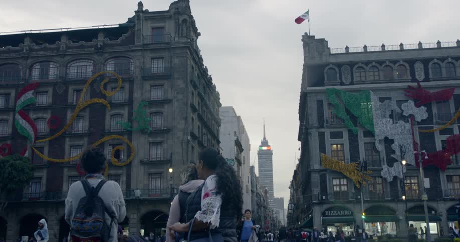 A mexican flag waving on top of building on the edge of a plaza