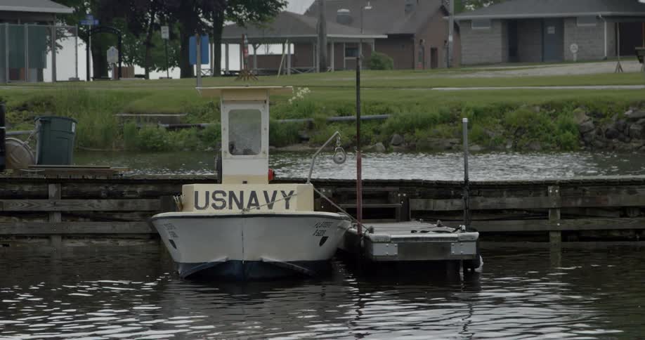 A small boat with us navy lettering is docked at a wooden pier