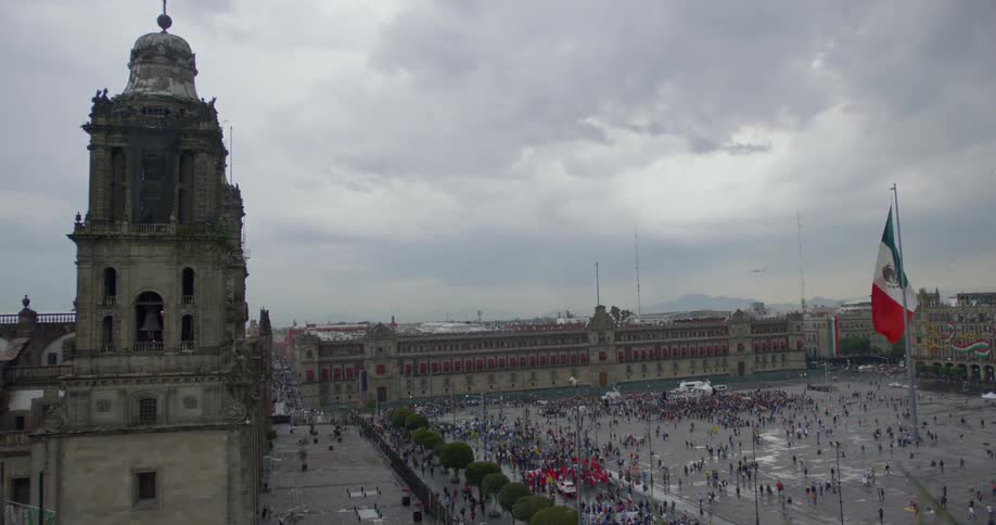 A city square with people and the mexican flag waving in the wind