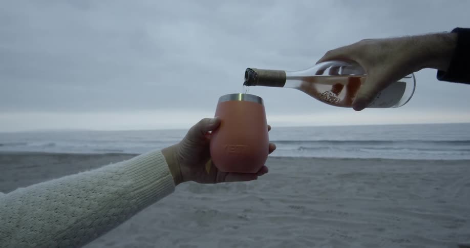 A man pours wine into a glass held by a woman on the beach