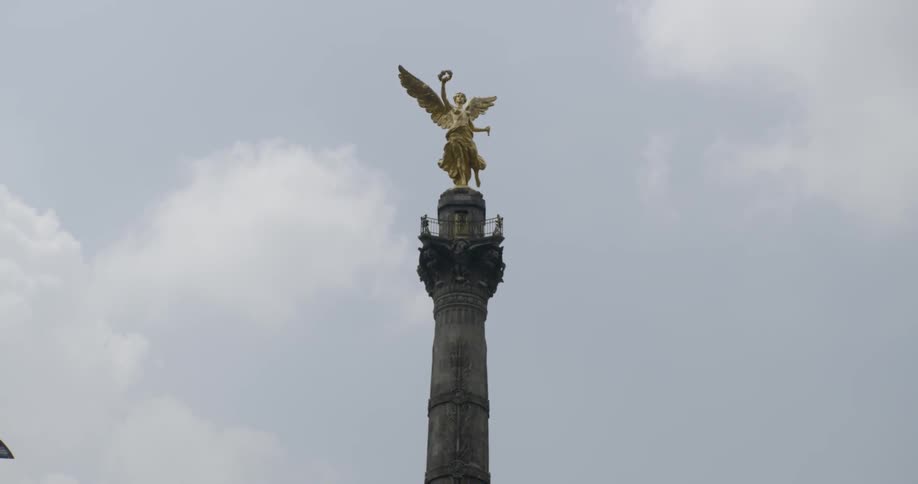 A sculpture of a golden angel holding a wreath on top of a tall sculpted pillar