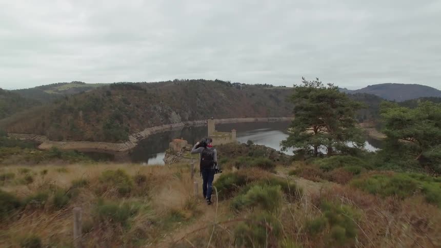 A man walks with a camera hikes towards a river