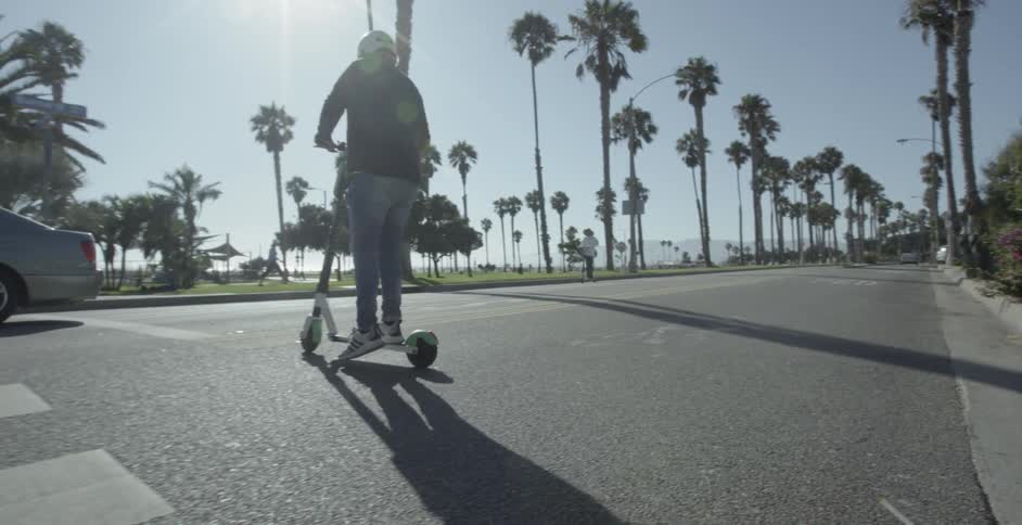 A person crosses the street on a scooter