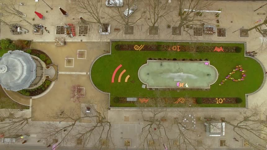 People walk on a town plaza with a gazebo and a bocce court