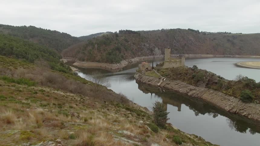 A male caucasian setting up a camera on a stand near mountains and a castle surrounded by water