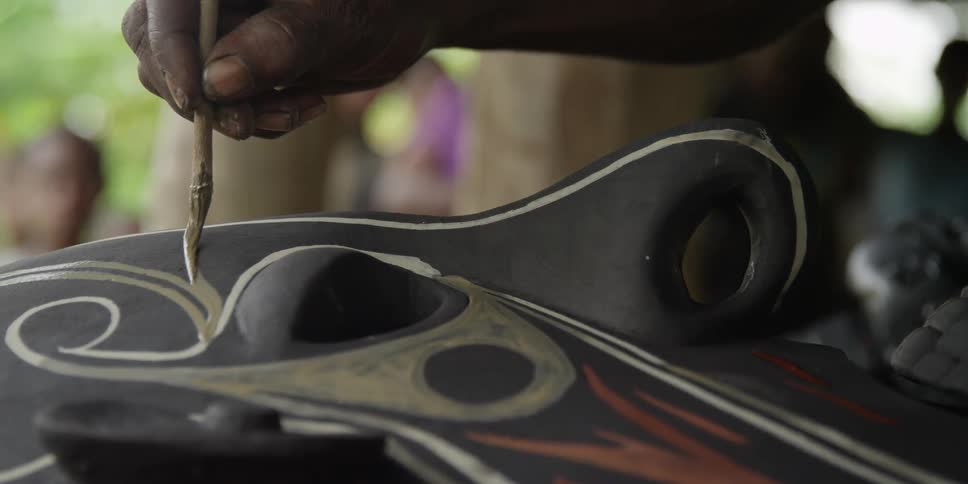 A person uses a brush to paint a decorative mask