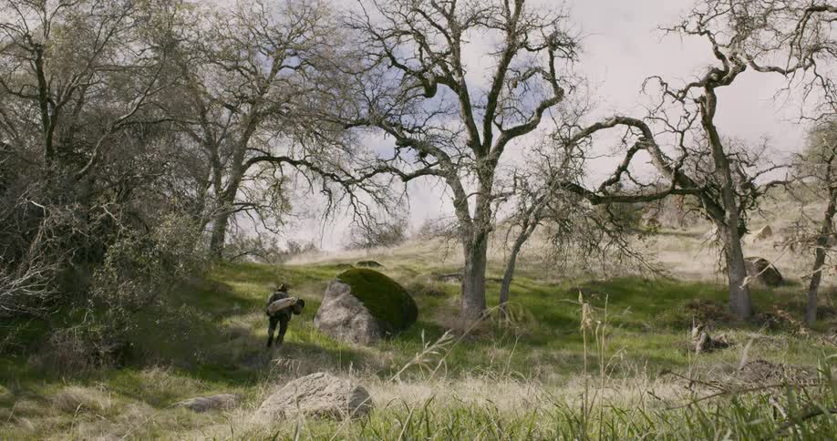 A man walking on grass with supplies on his back