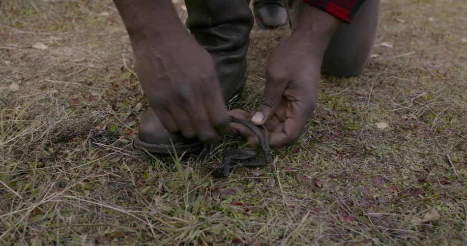 A black male setting a small trap outside on the grass