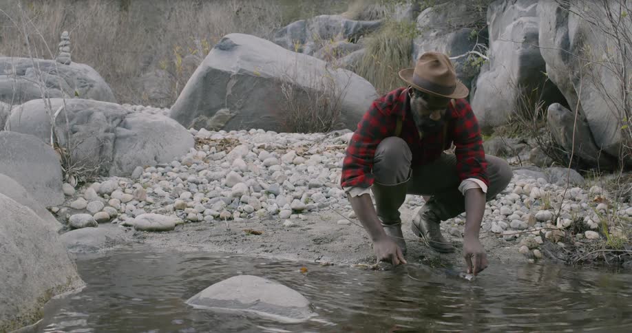 A man panning for gold in a creek surrounded by rocks and boulders