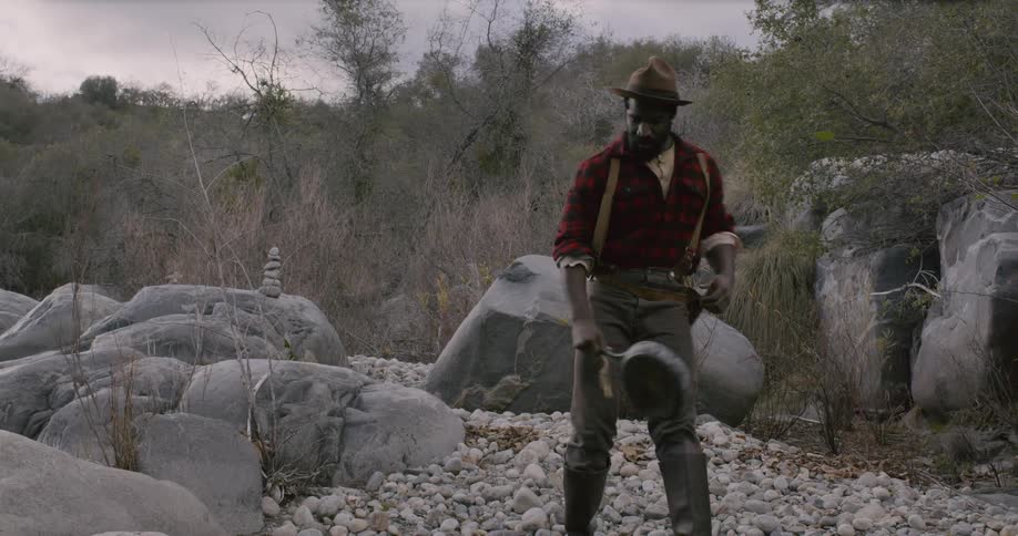 A black male carrying a pan to a water source then scoops up dirt