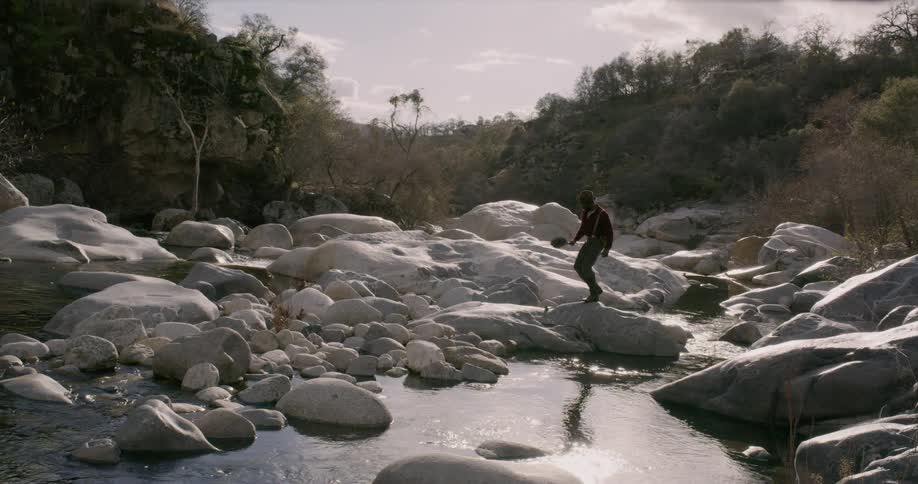 A man walks over large rocks covering a small creek